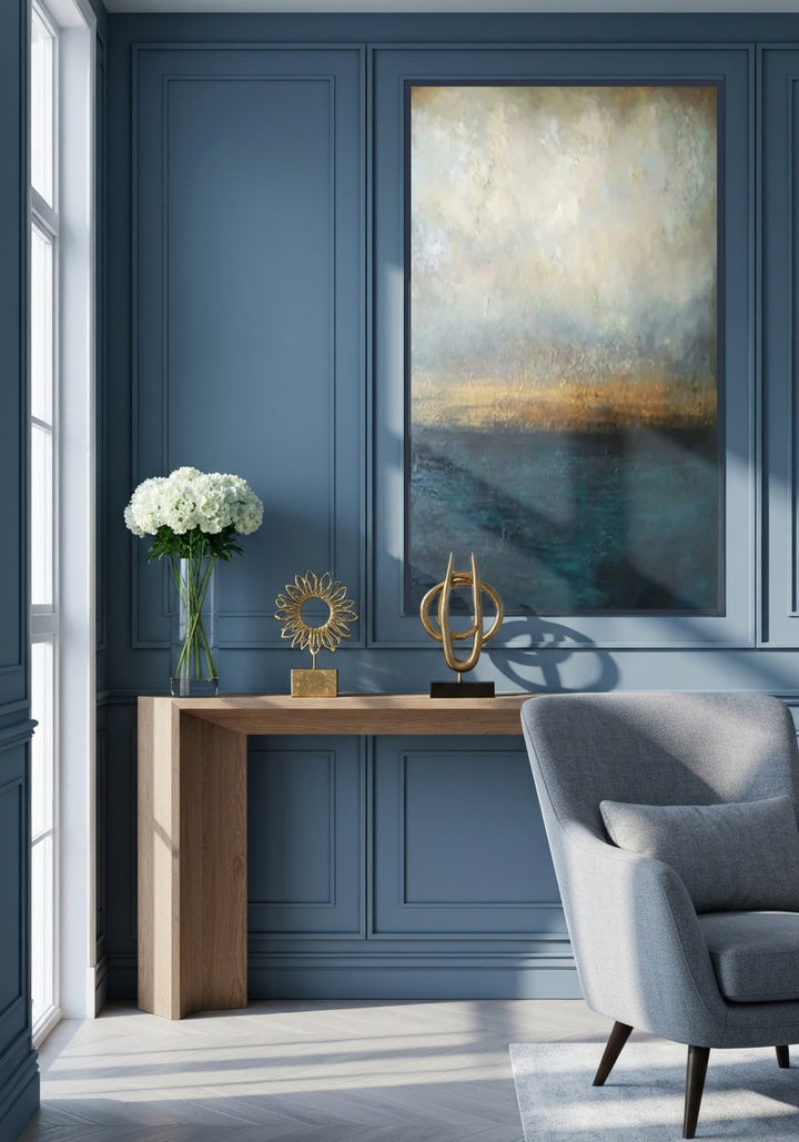 Modern interior with blue paneled wall, gray armchair, wooden console table, and abstract painting.